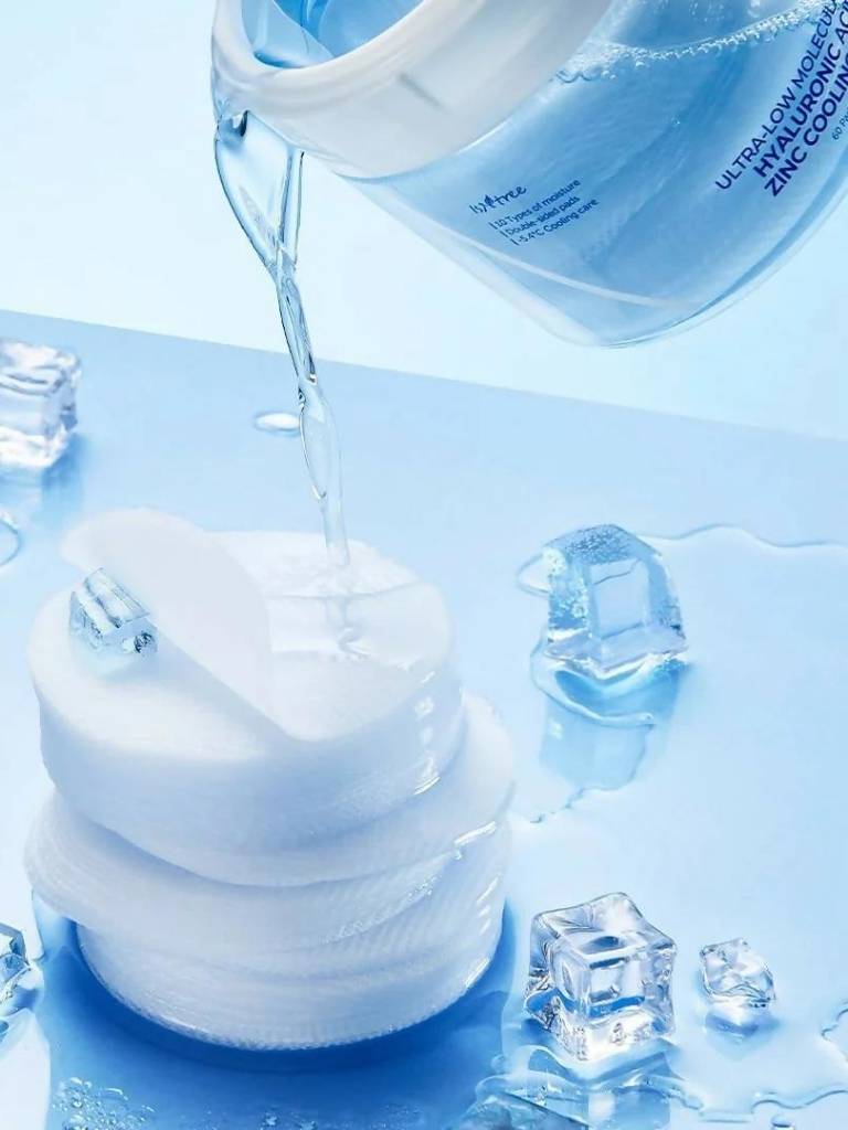 Skincare product with water being poured over it, surrounded by ice cubes on a blue background