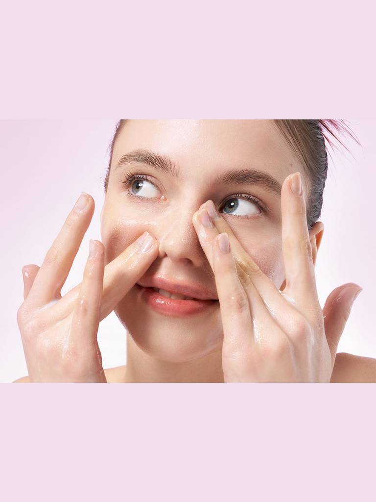 Woman applying cream to her face with a pink background
