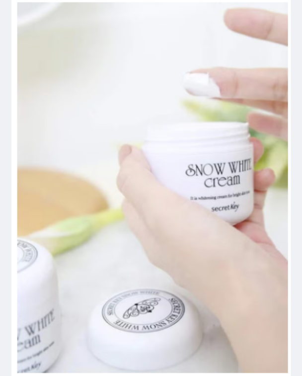 Hand holding a jar of Snow White cream with a blurred background