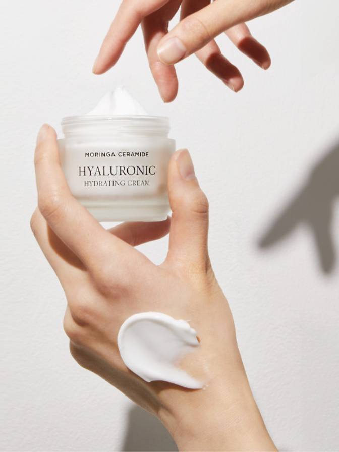 Hand holding a jar of Moringa Ceramide Hyaluronic Hydrating Cream with a small amount on the palm.