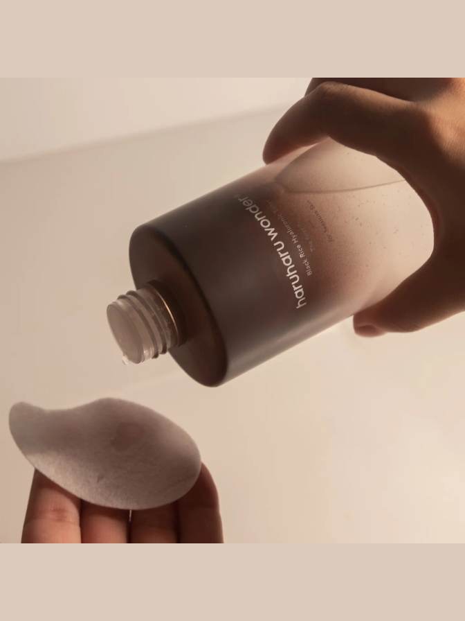Hand holding a brown bottle labeled 'harmo' over a beige background