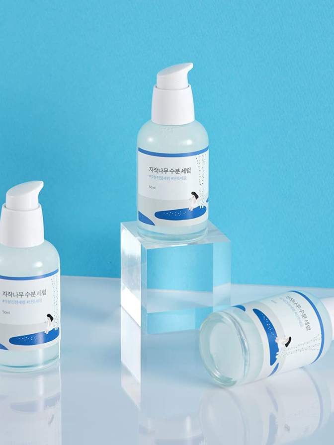 Three skincare bottles with blue labels on a reflective surface and blue background
