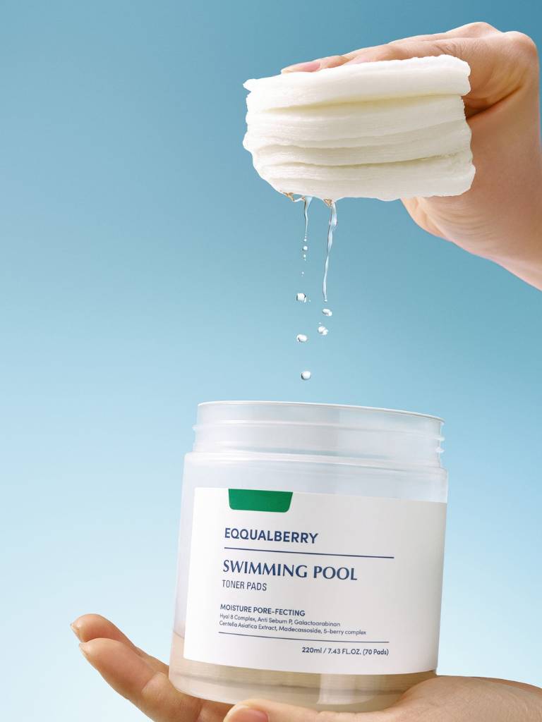 Hand holding a container of Equalberry swimming pool toner pads with a blue background