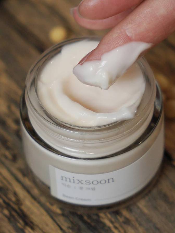 Jar of cream with a hand applying some to the lid, on a wooden surface.