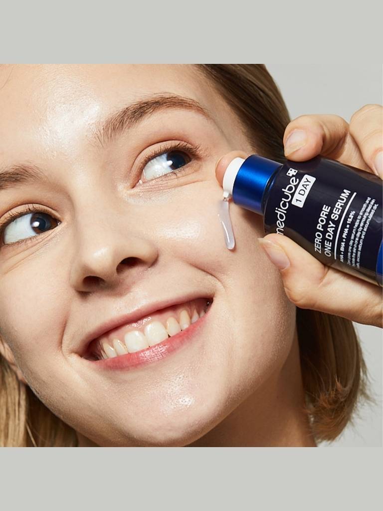 Person applying Medicube serum to their face with a neutral background