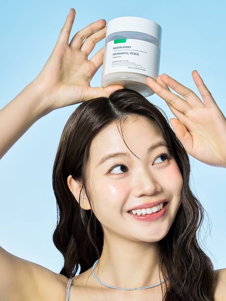 Woman holding a skincare product above her head against a blue background