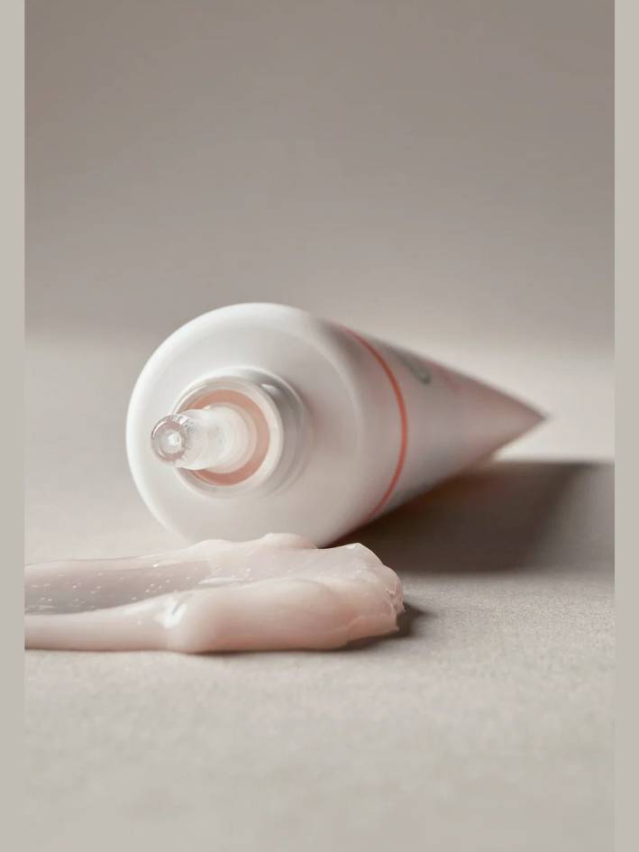 Tube of cream with a visible amount of cream on a neutral background