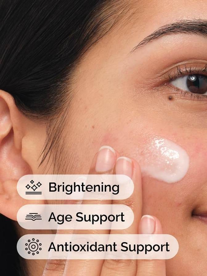 Close-up of a person applying cream to their face with text indicating brightening, age support, and antioxidant support.