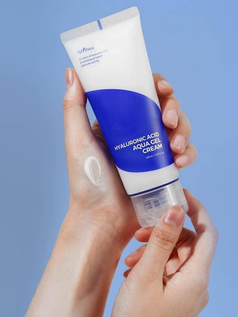 Hand holding a tube of hyaluronic acid cream against a blue background