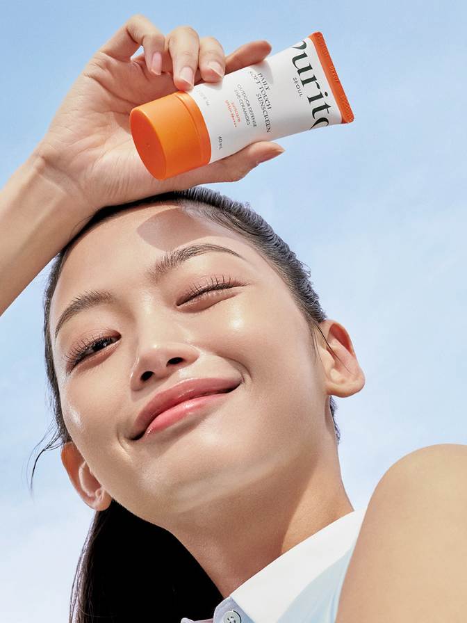 Person applying sunscreen cream to their face with a clear blue sky background