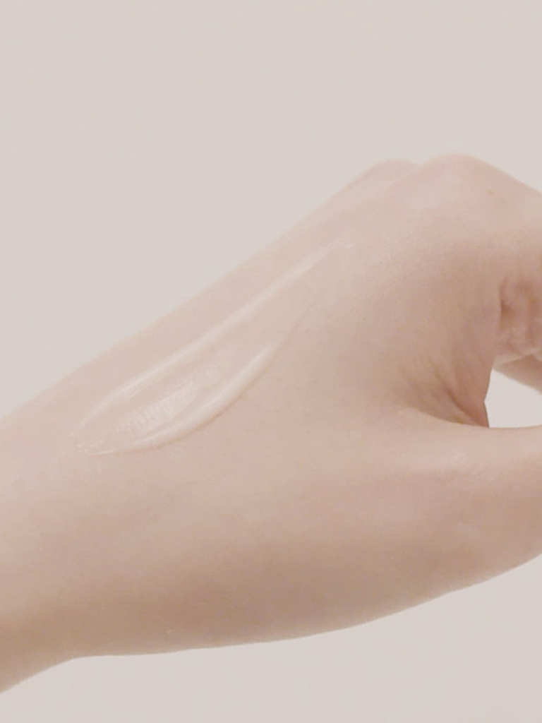 Hand applying a clear cream or lotion on a light background
