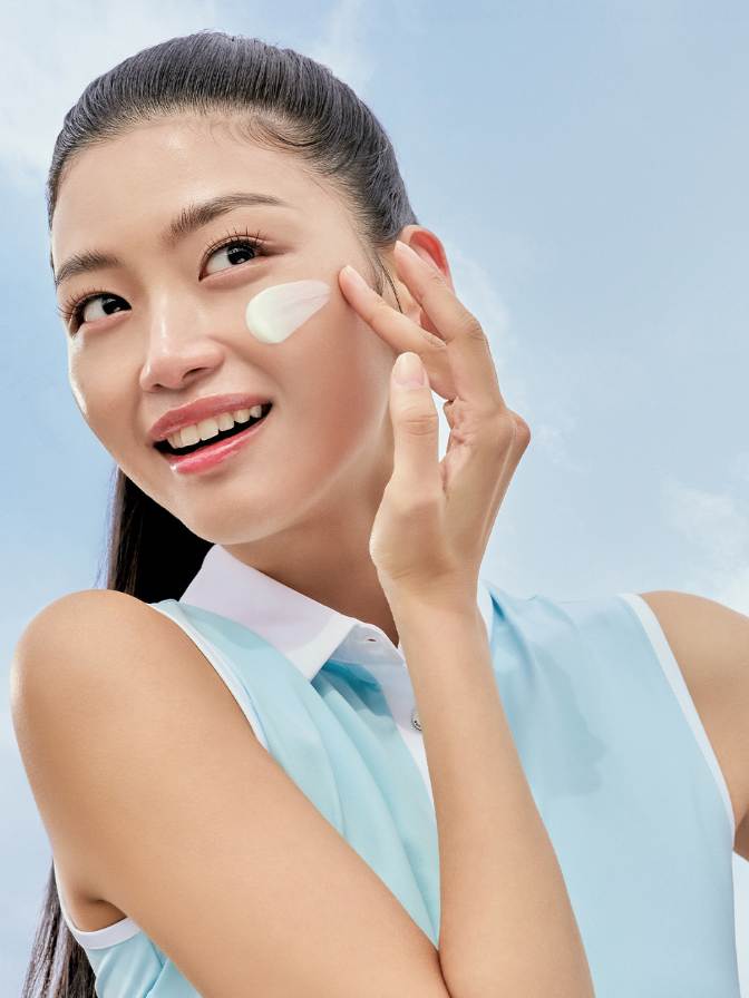 Woman applying cream to her face against a light blue background