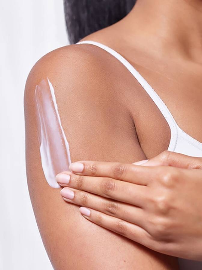 Person applying a white cream or lotion to their shoulder against a plain background