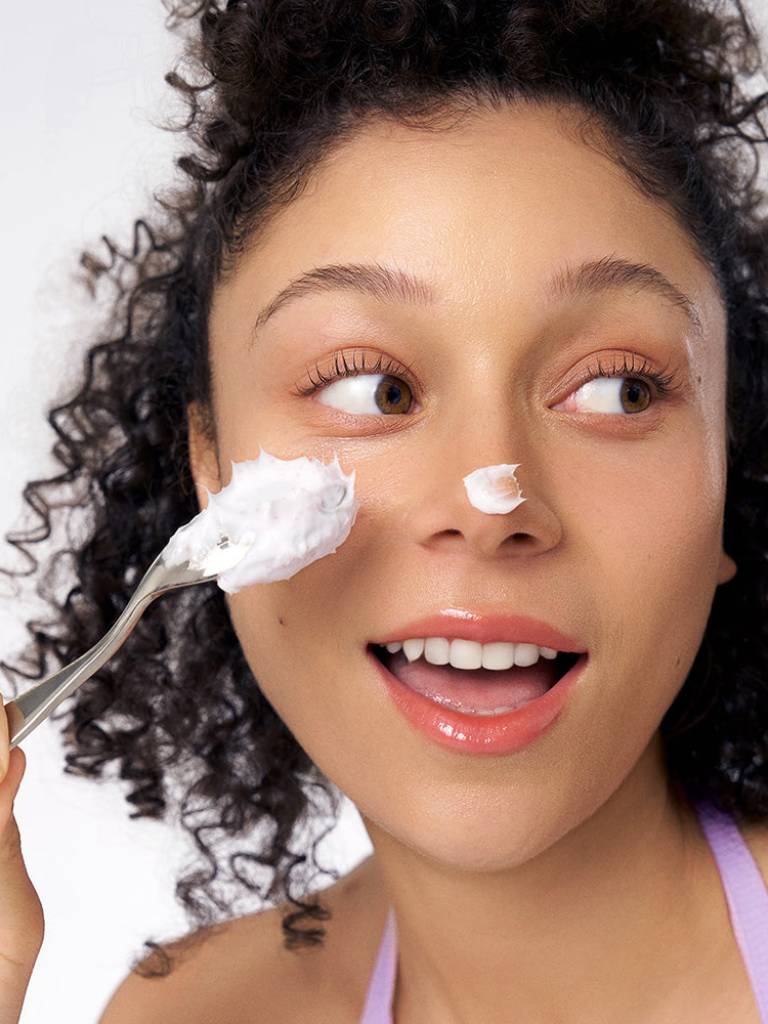 Person applying a white cream to their face with a spoon