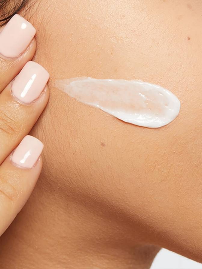 Close-up of a hand applying a small amount of cream to skin