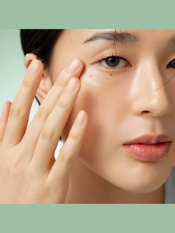 Close-up of a person applying skincare product to their face with a green background