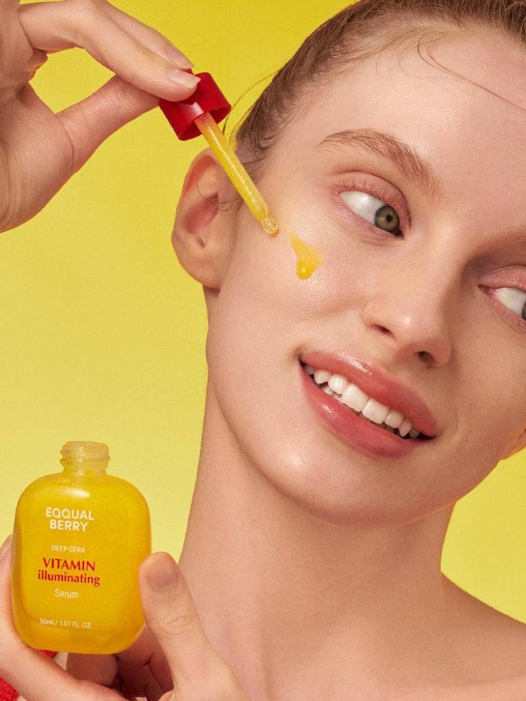 Person applying a yellow skincare serum to their face with a dropper against a bright yellow background.