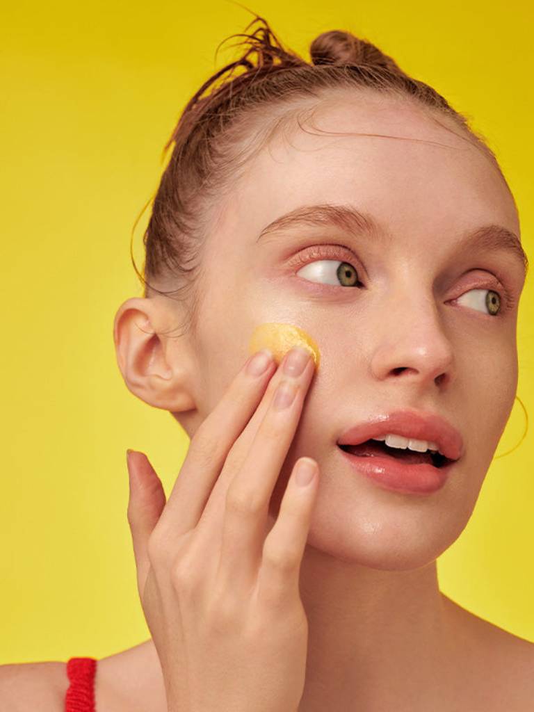 Woman applying sunscreen on a yellow background