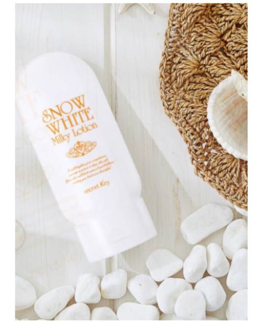 Snow White body lotion on pebbles with a woven mat in the background