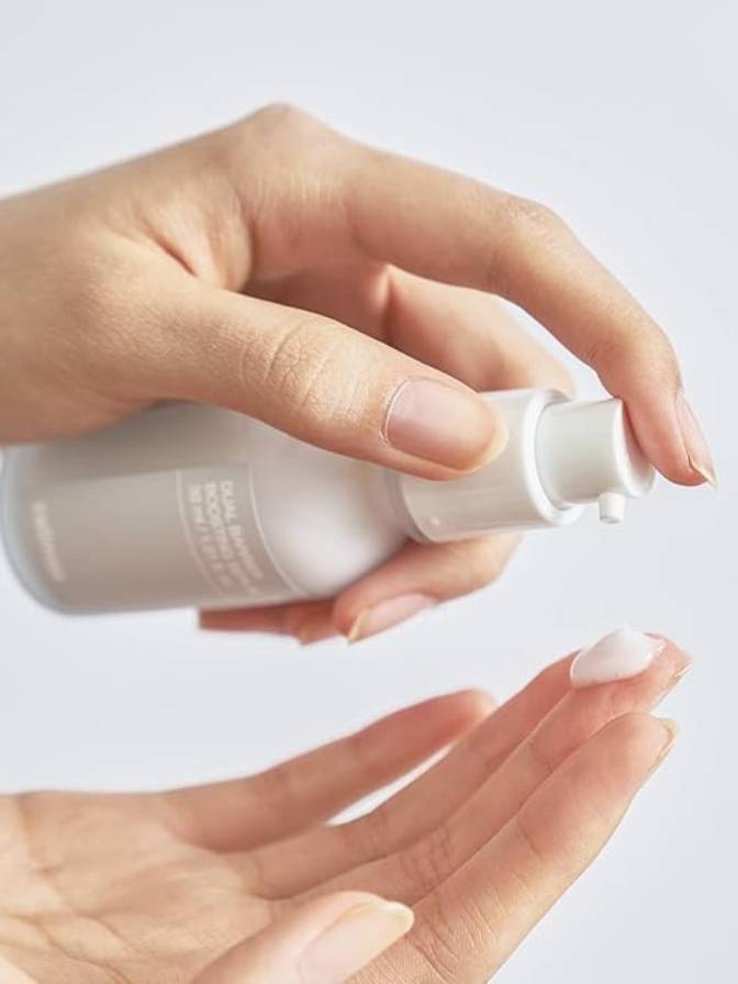 Hand holding a white skincare bottle with a pump on a light gray background
