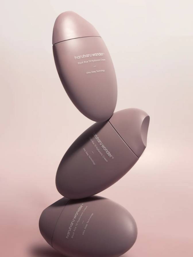 Three pink skincare bottles stacked on a light pink background