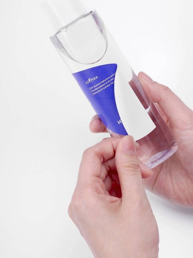 Hand holding a clear bottle with a blue label against a white background