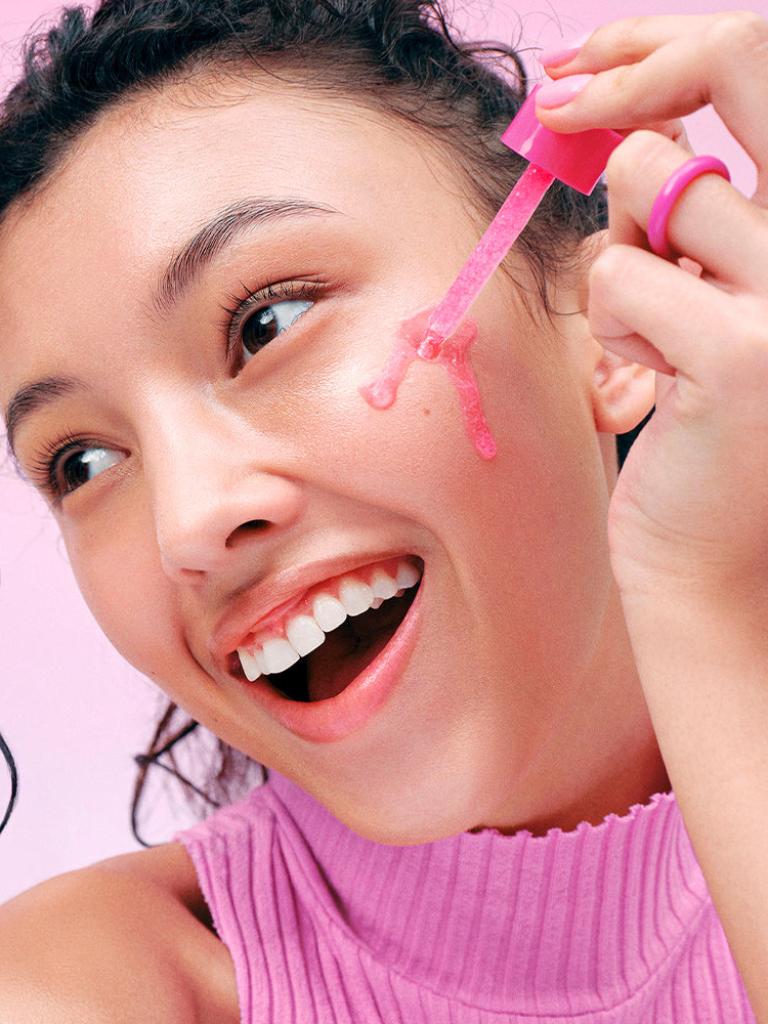 Person applying pink gel to their face with a brush against a pink background