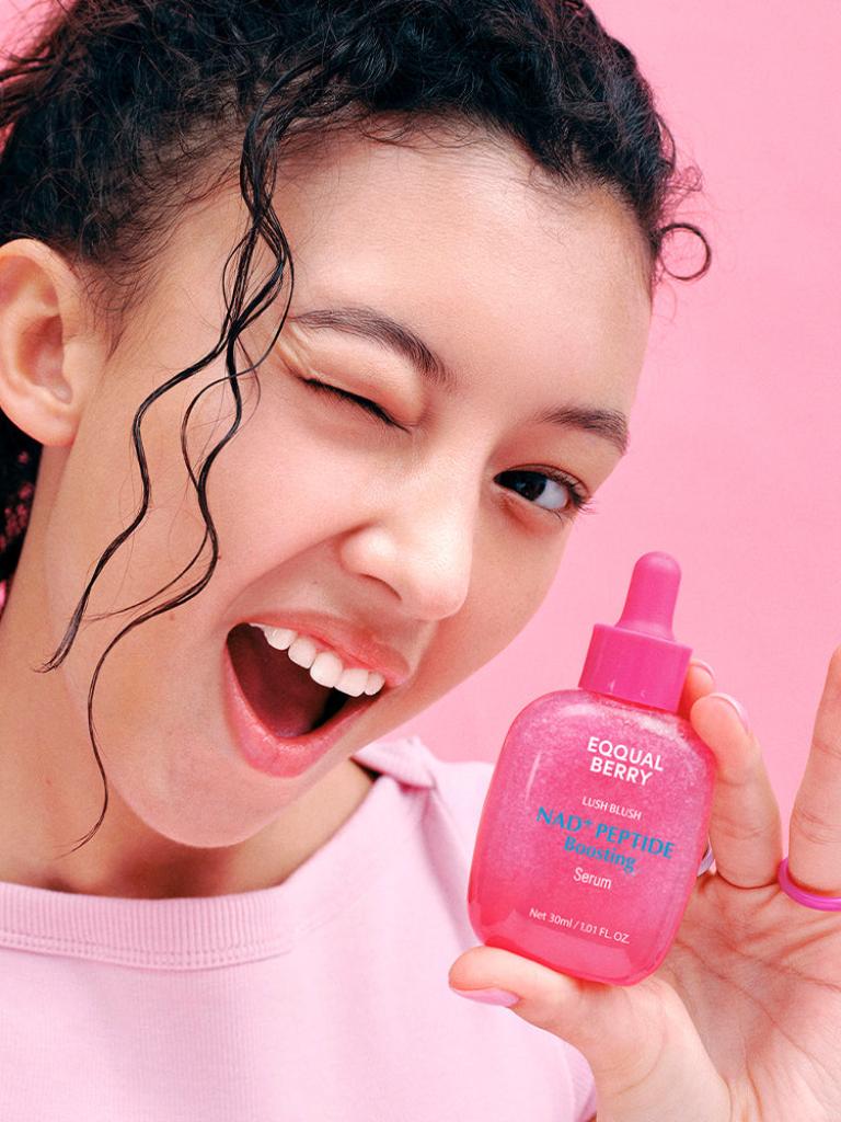 Person holding a pink bottle with a visible brand "Eqqualberry' logo against a pink background