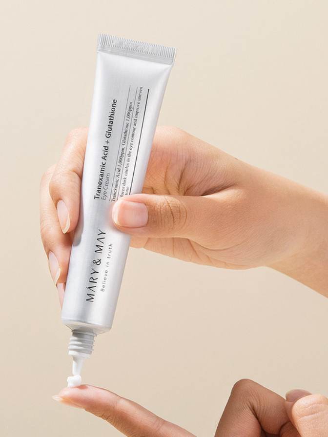 Hand holding a tube of Mary & May skincare product against a beige background