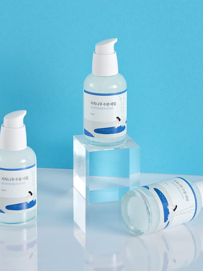 Three skincare bottles with pump dispensers on a reflective surface against a blue background