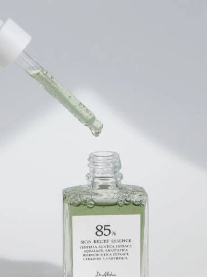 Glass bottle of '85% Skin Relief Essence' with a dropper on a light gray background