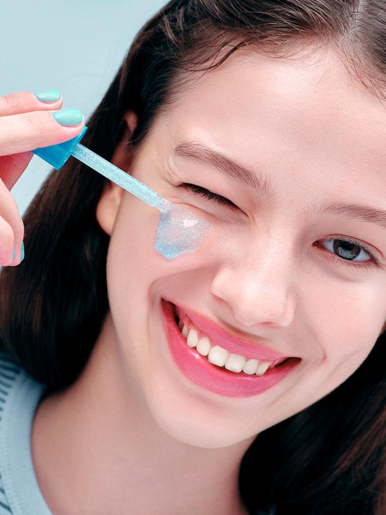 Woman applying a clear gel or cream under her eye with a blue applicator.