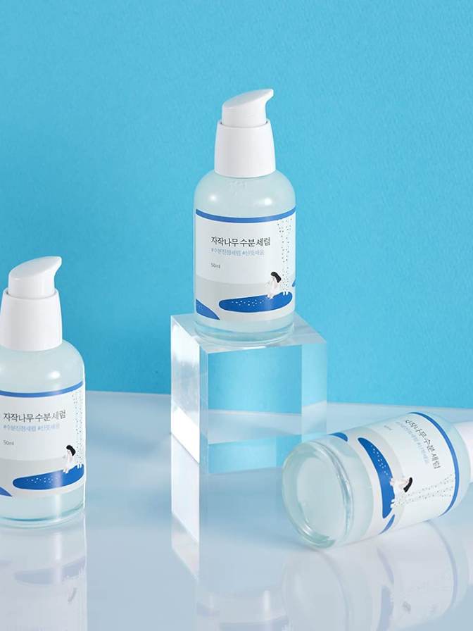 Three skincare bottles with pump dispensers on a reflective surface against a blue background