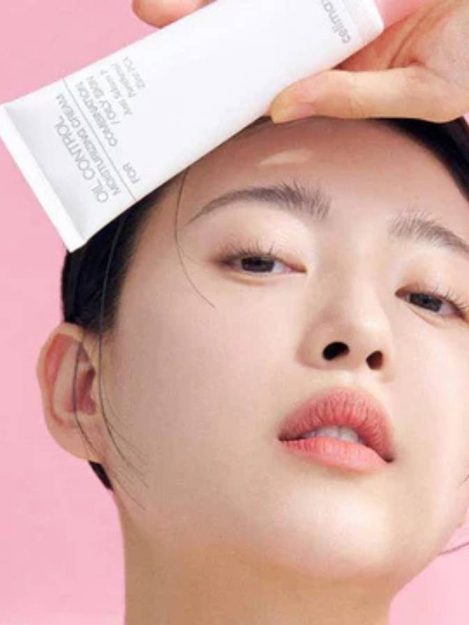 Person holding a skincare product over their face against a pink background