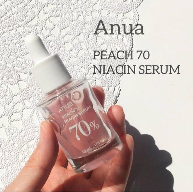 Hand holding a bottle of Anua Peach 70 Niacin Serum against a light background