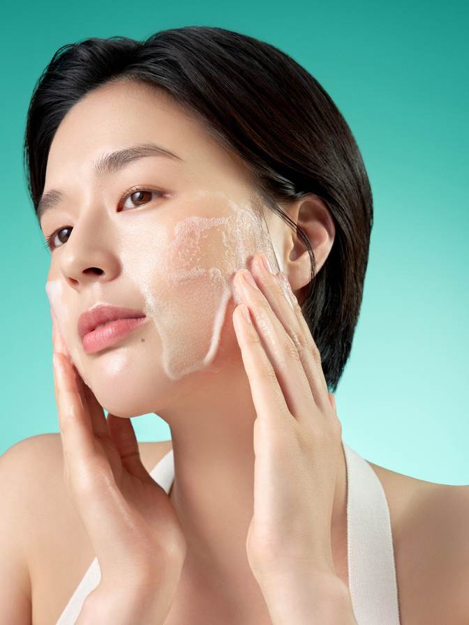 Woman applying a facial mask with a teal background
