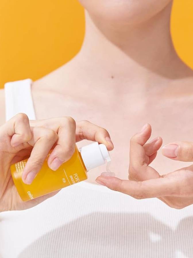 Person applying a yellow bottle of skincare product to their hand against a white background