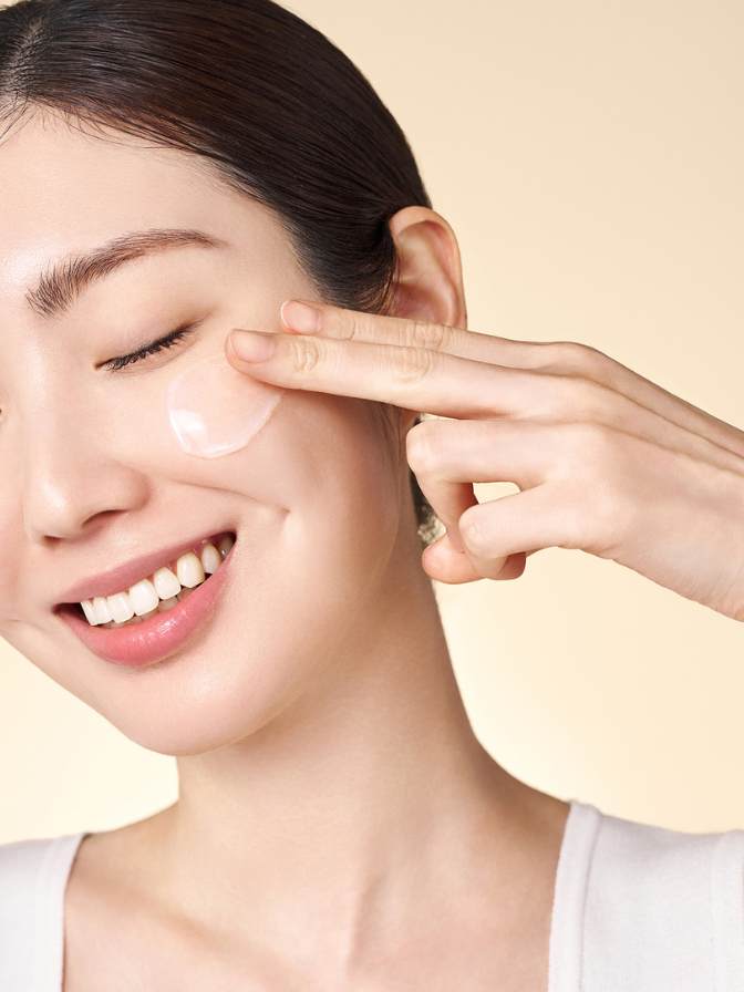 Woman applying cream to her face with a neutral background