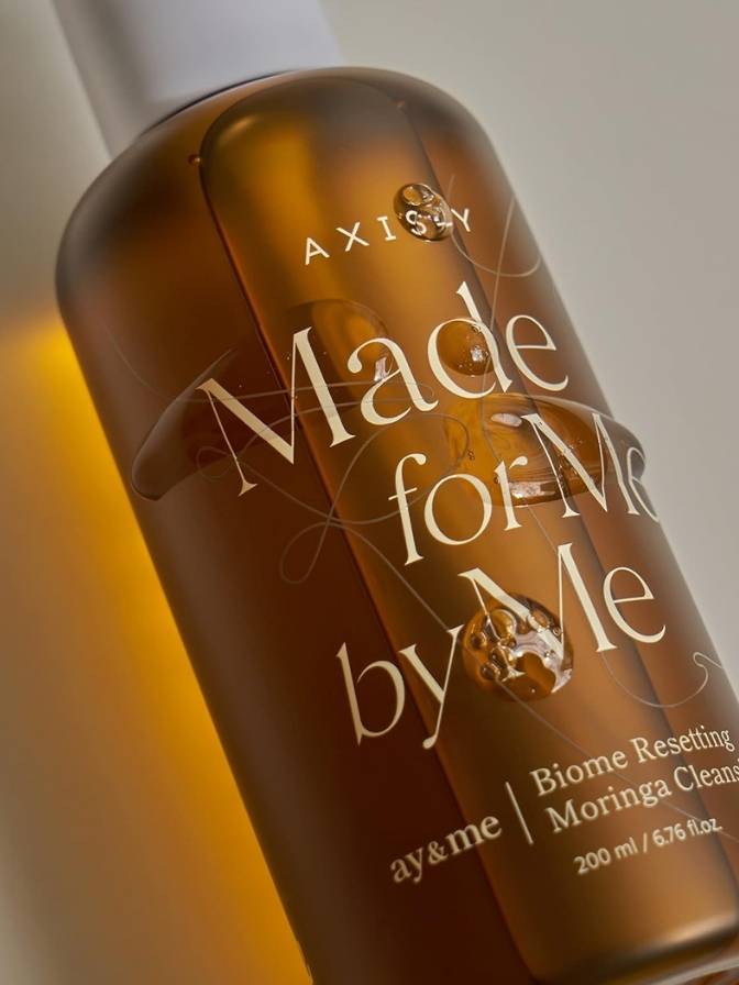 Bottle of Axiology skincare product with 'Made for Me by Me' text on a neutral background