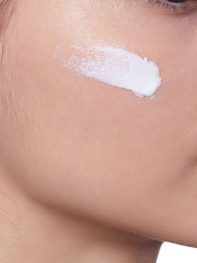 Close-up of a person applying white cream to their face