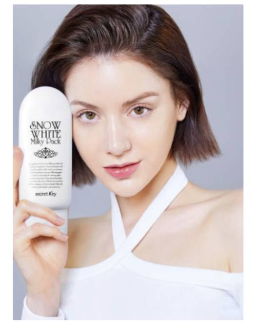 Woman holding a skincare product with a plain background