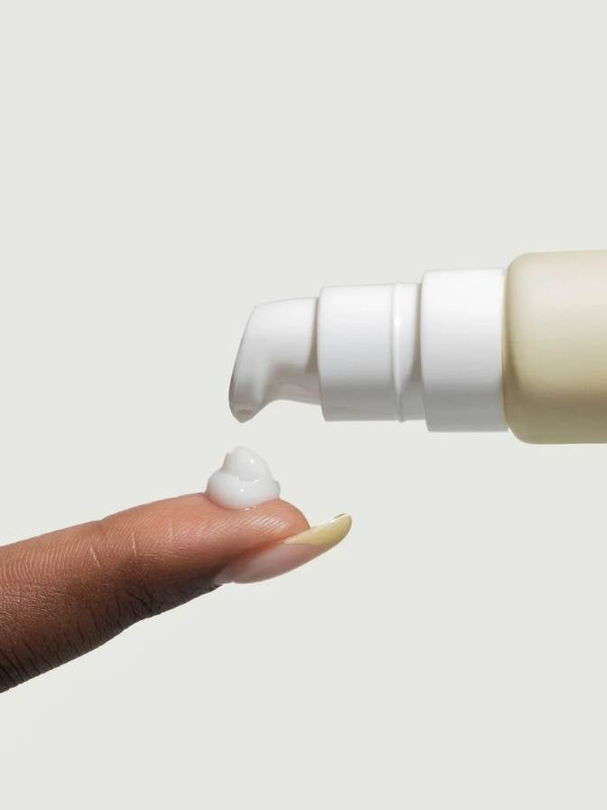 Hand holding a white bottle with a pump against a light gray background