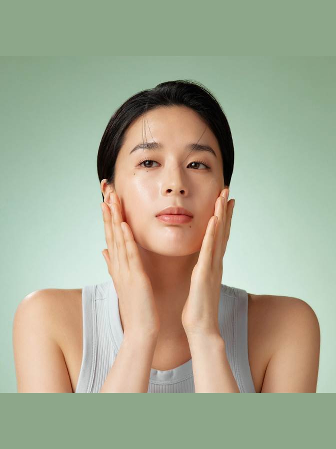 Woman touching her face against a light green background