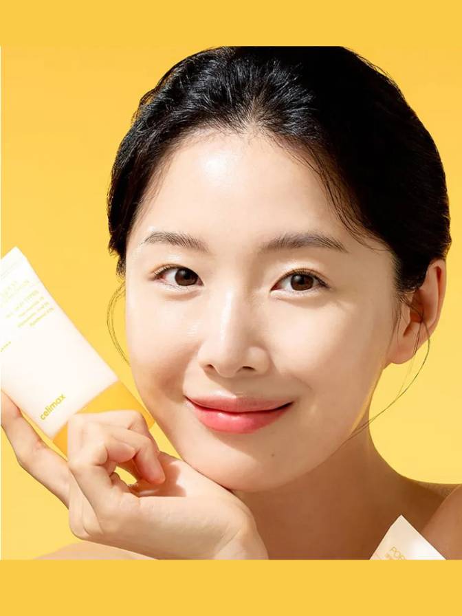 Woman holding a skincare product against a yellow background