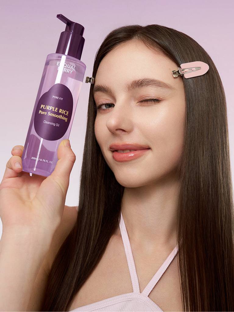 Woman with straight hair holding a bottle of 'Purple Rice' product against a light purple background